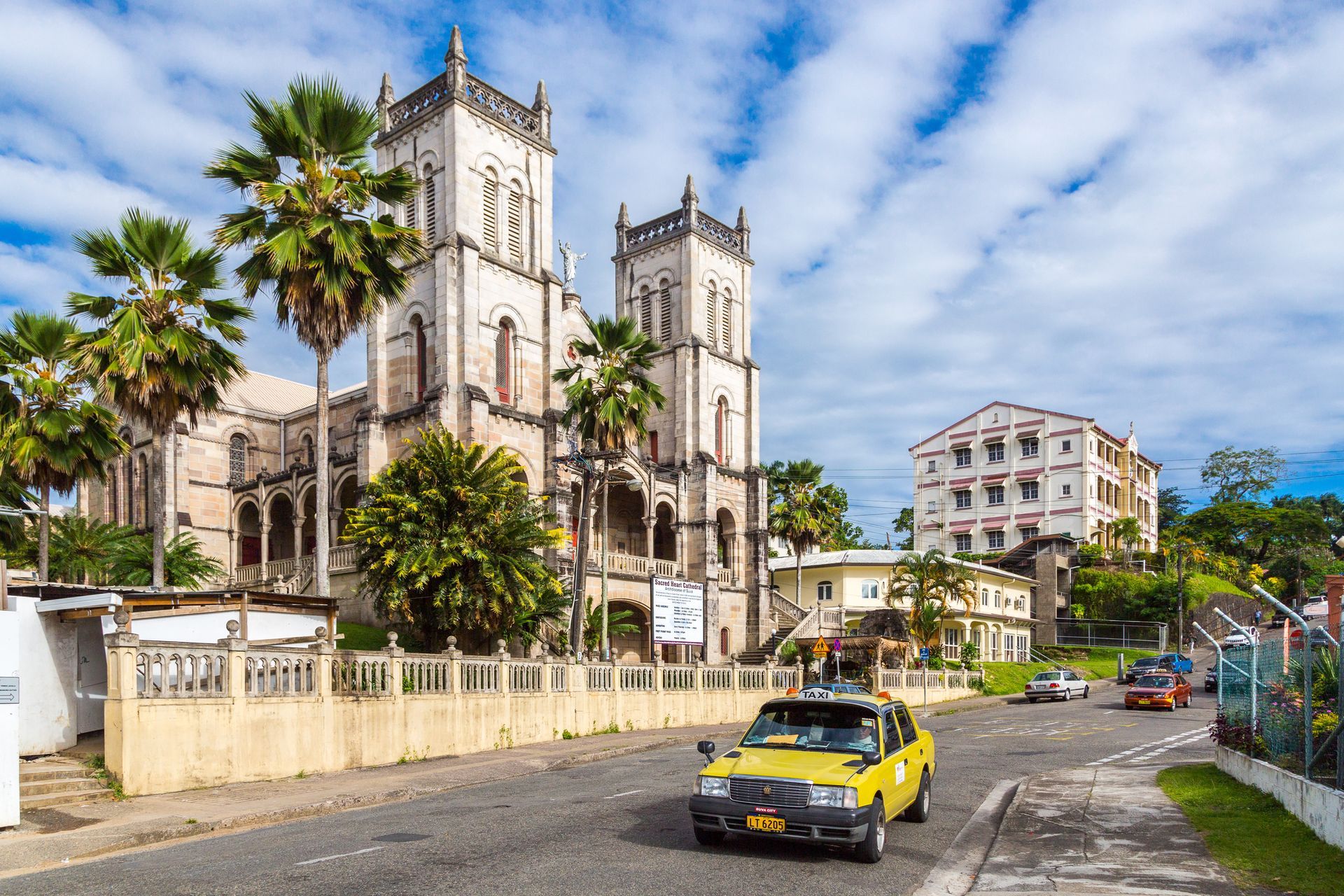 Colonial-era stone buildings and palms on a Suva street with a passing taxi
